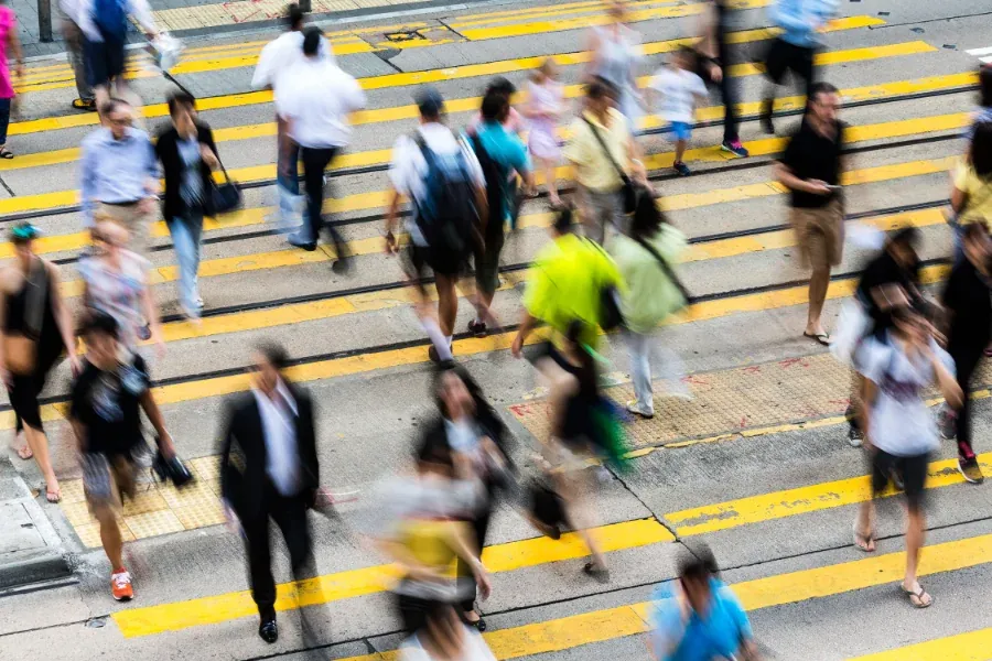 A crowd of people crossing a busy city street, shot from above with their movement blurred