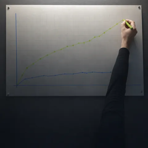 A hand drawing a rising line on a chart pinned to a wall